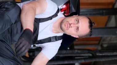 Özel üniformalı yorgun bir araba tamircisi oturup işten dinlenir. Zor bir gündü. Dikey video.