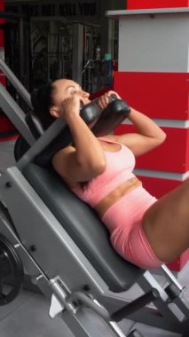 Sportif kadın spor salonundaki egzersiz makinesinde bacak kaslarını çalıştırıyor. Güzel seksi vücudu olan şık bir kadın. Dikey video