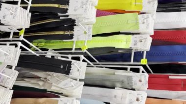 Farklı beden ve renkte giysiler için pek çok farklı fermuar, bir giyim atölyesinin atölyesindeki raflara yıldırımlar konuyor. Dikey video