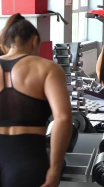 Sportif kadın kol kaslarını çalıştırmak için ağır dambılları kaldırır. Spor salonundaki bir sporcunun portresi. 4k video. Dikey video