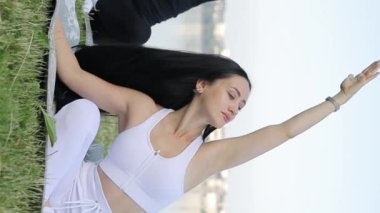 Güzel kadınlar yoga yapıyor ya da gölün yakınındaki yeşil çimlerde geriniyor. Sabah antrenmanındaki spor kızları. Dikey video