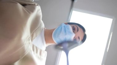 Dişçi muayenehanesinde çalışan bir dişçinin en iyi görüntüsü. Diş tedavisi sırasında maske takan bir dişçi. Dişlerin tam zamanında tedavi edilmesi. Dikey video