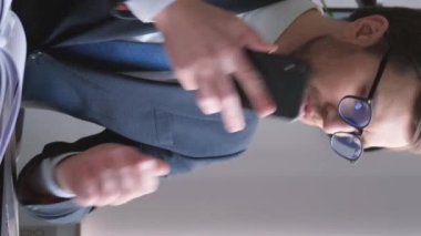 Amerikan görünümlü genç bir yatırım bankacısı bilgisayar üzerinde çalışırken telefonla konuşuyor. Meşgul müdür. Ofiste çalış. Dikey video