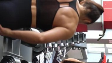 Sportif kadın kol kaslarını çalıştırmak için ağır dambılları kaldırır. Spor salonundaki bir sporcunun portresi. 4k video. Dikey video