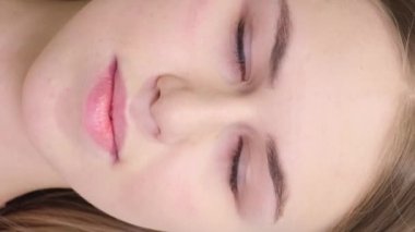 Güzel bir genç kızın portresi. Genç, sarışın bir kız açık bir arka planda dururken kameraya bakıyor. Dikey video