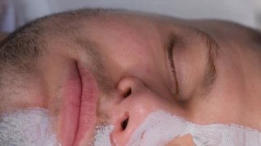 Bir adamın yüzüne maske takarken bir adamın yüzüne yakın çekim. Kozmetikçiyle randevusu olan bir adam, bir dermatolog. Erkek cilt bakımı. Dikey video