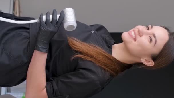 在美容院工作时 快乐地微笑着美丽的美容师女孩 美容师在美容外科诊所恢复活力的过程中的男人美容师在工作 垂直录像 — 图库视频影像