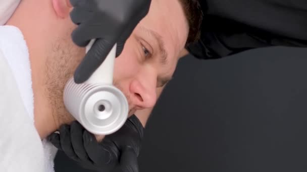 用现代电按摩器对一个年轻貌美的男人进行面部按摩 男性恢复美容术的活力 垂直录像 — 图库视频影像
