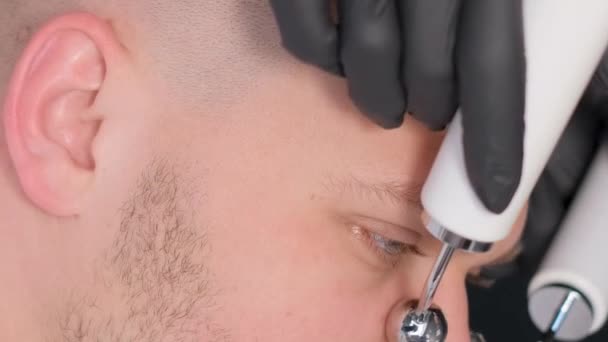 美容师的特写会让一个有魅力的年轻人用电动振动器做面部按摩 男性恢复美容术的活力 皮肤年轻化 垂直录像 — 图库视频影像