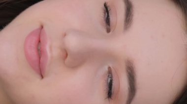 Gülümseyen genç ve güzel bir esmer kızın yüzüne yakın çekim. Esmer bir kadının portresi. Dikey video