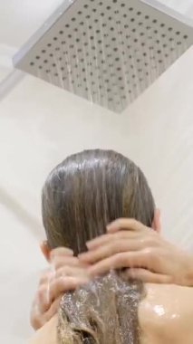 Güzel genç bayan duşta eğleniyor. O, duşta saçını yıkar. Dikiz aynası. Dikey video