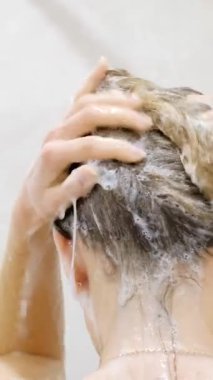 Saçını şampuanla yıkayan bir kadın. Uzun saçlar duş alıyor. Dikey video.