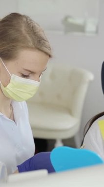 Dişçi randevusundaki genç esmer kız. Beyaz diş implantı kurulumu. Bir dişçinin işi. Dikey video
