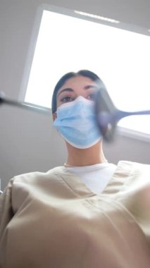 Dişçi muayenehanesinde çalışan bir dişçinin en iyi görüntüsü. Diş tedavisi sırasında maske takan bir dişçi. Dişlerin tam zamanında tedavi edilmesi. Dikey video