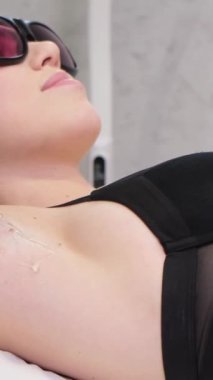 Epilasyon için hazırlık. Bir kozmetolog, genç bir kızın koltukaltlarını tahta bir sopayla sarıyor. Güzel bir vücudu önemsemek. Dikey video