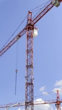 Mavi gökyüzü arka planında yüksek katlı bir vinç ile inşaat işi. Yeni evlerin inşaatı. Dikey video