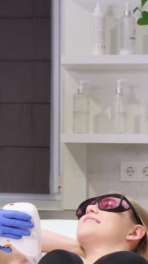 Bir kadının koltuk altlarındaki kılların alınması prosedürü. Bir kozmetik uzmanı güzellik salonunda lazer cilt gençleştirme ameliyatı yapıyor. Yüz bakımı. Dikey video