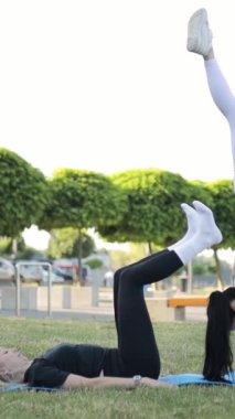 Temiz havada fitness egzersizleri. Genç kadınlar bacak esnetme egzersizleri yapıyor, sağlık eğitimi alıyor. Dikey video