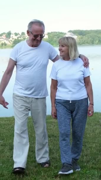 アクティブ幸せな成熟したカップル スポーツウェアで話した後朝の運動 ウォームアップ 湖の近くに立って バーティカルビデオ — ストック動画