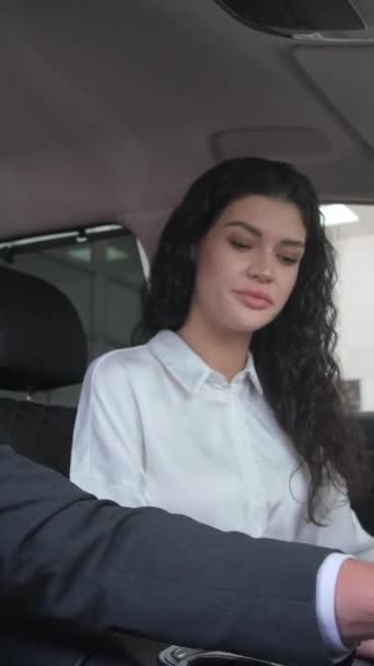A beautiful brunette girl chooses a new car at a car dealership. A woman examines the interior of a car. The girl is delighted with the new car. Vertical video