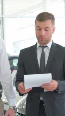 Hoş bir çift araba galerisinden araba alırken müdürle konuşuyor. Araba galerisi. Dikey video