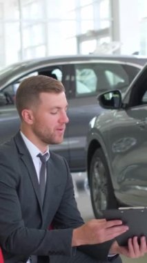 Hoş bir çift araba galerisinden araba alırken müdürle konuşuyor. Araba galerisi. Dikey video