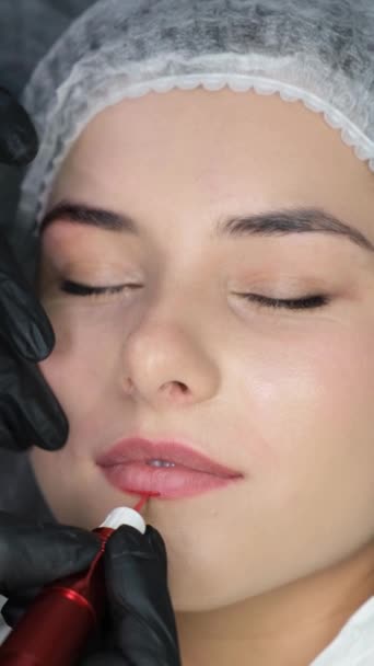 美容师把永久化妆品涂在嘴唇上 年轻美丽的女人有永久化妆品纹身在她的唇 垂直录像 — 图库视频影像