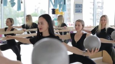Beden eğitiminde pilates yapan bir grup insan, kollarını kaldırmış toplarla denge kuruyor, kaslarını geliştiriyor. Sağlıklı spor yaşam tarzı, grup sınıfında fitness.