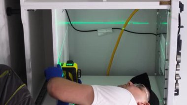 Bir adam odaların mutfağına yerleştirmek için lazer seviyesini kesin ölçümler için kullanır. Boyunu lazer seviyesiyle ölç. Lazer seviyesi. Dikey video