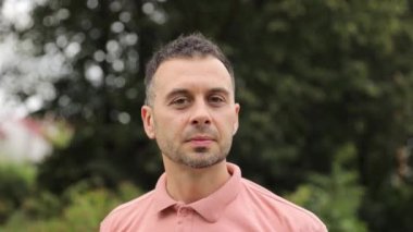 Avrupa görünümlü bir adamın portresi bulanık ağaçların arka planında kameraya bakıyor..