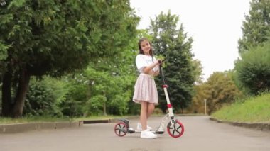 Küçük bir kız elektrikli scooter sürmeyi öğreniyor. Şehir parkında scooter sürmek..