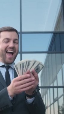 Başarılı bir iş adamı cam iş merkezinin arka planında dolar sayar. Başarı, servet, kariyer gelişimi, lotoyu kazanmak. Dikey video