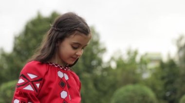 Güzel kırmızı işlemeli elbiseli küçük bir Ukraynalı kız yeşil bir parkta yürüyor. Ukraynalı çocuklar.