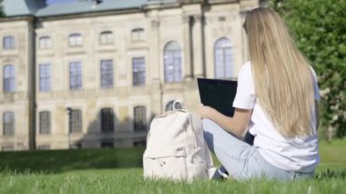 Dışarıdaki çimlerin üzerinde oturan genç kız üniversite geçmişinde dizüstü bilgisayar kullanıyor. Üniversitede okuyorum..