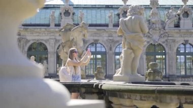 Turist bir kız, Avrupa 'daki bir sarayda akıllı bir telefonla taş heykellerin fotoğraflarını çekiyor. Turist seyahat kavramı.