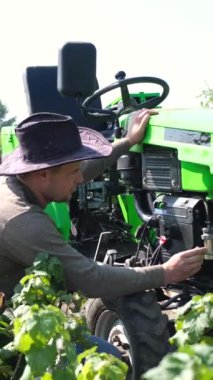 Genç bir çiftçi tarlanın ortasında küçük bir traktörü tamir ediyor. Tarlada kırsal bir işçi. Dikey video