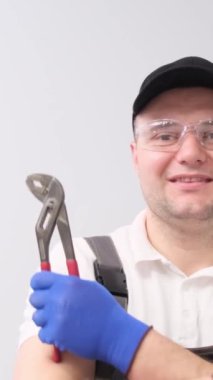 İngiliz anahtarı olan profesyonel tesisatçı, gülümsüyor ve stüdyoda beyaz arka planda poz veriyor. Dikey video