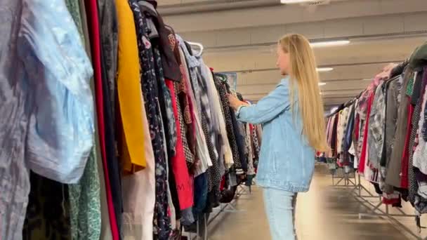 아름다운 여자는 트렌디 쇼핑몰에서 옷걸이에 다채로운 옷걸이를 — 비디오