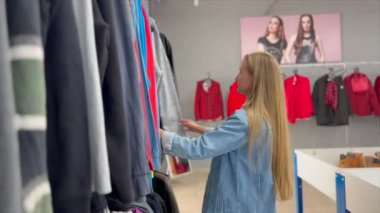 Genç bir kadın kadın mağazasında kıyafetlere bakar. Kıyafet alışverişi. Sonbahar giysi koleksiyonu.