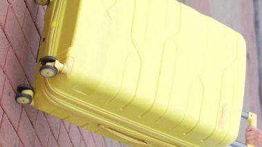 Tanımlanamayan bir kadın gezgin elinde sarı bir bavulla tramvay raylarının yanında yürüyor. Turizm reklamı. Dikey video.