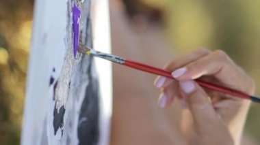 Yetenekli genç bir kadın, güzel bir sonbahar ormanındaki tuvale fırça ve akrilik boya kullanarak resim çiziyor. Dikey video.