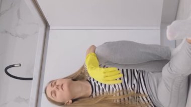 Temizliği bitirdikten sonra ev hanımı temiz zeminde eldiven ve paspas ile otururken uykulu hissediyor. Temizlikten sonra yorgun bir kadın. Dikey video.