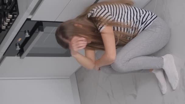 月経痛に苦しむ疲れた女性は キッチンルームの床に座っている 月経サイクル バーティカルビデオ — ストック動画