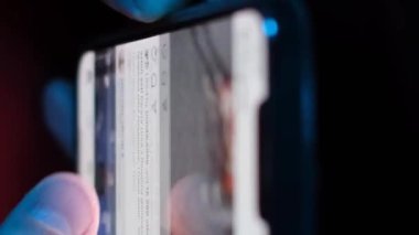 Genç bir adam cep telefonuyla sosyal ağları tarıyor, yakın plan. Rahat yetişkin erkek, modern dijital yaşamı somutlaştırmak için geceleri cep telefonunda uygulamalar okur. Dikey video.