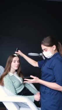 Kozmetoloji kliniğinde genç bir kadın hastanın kafa derisinin ve saç foliküllerinin trikolojik ve dermatolojik incelemesi. Saç problemleri. Kırılgan ve kuru saçlar. Dikey video.