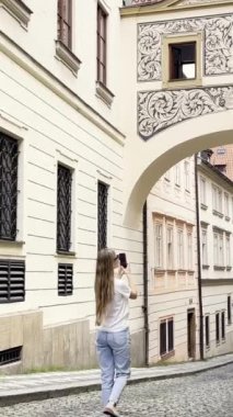 Prag caddesinde yürüyen genç bir kadın telefonuyla mimarinin fotoğraflarını çekiyor. Turizm kavramı. Dikey video