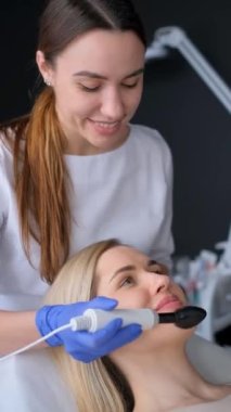Güzellik uzmanımız güzellik salonunda genç bir bayana masaj yapıyor. Profesyonel yüz tazeleme. Dikey video. 