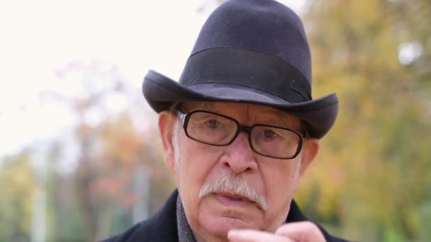 秋の公園に立っている間メガネを調整する帽子で祖父の肖像画 — ストック動画