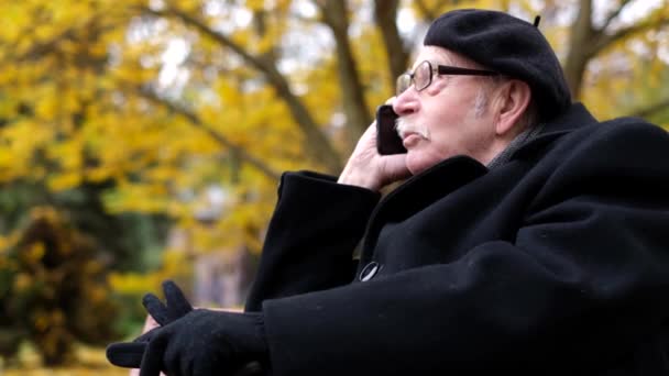 Uomo Anziano Con Berretto Nero Siede Una Panchina Parco Autunnale — Video Stock