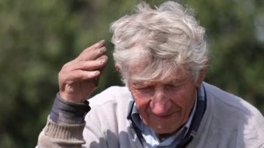 Saçlarını elleriyle düzelten ve kameraya bakan yaşlı, kır saçlı bir büyükbabanın portresi. Yaşlı adam 90 yaşında.